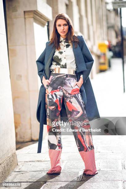 Landiana Cerciu wears a white shirt with black patterns ; a petrol-blue round-edges kimono-style coat ; a golden belt ; a red shoulder-bag with...