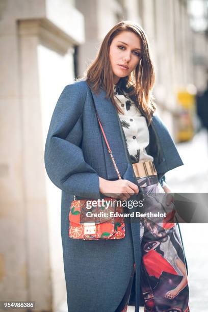 Landiana Cerciu wears a white shirt with black patterns ; a petrol-blue round-edges kimono-style coat ; a golden belt ; a red shoulder-bag with...