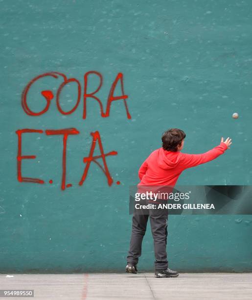 Kid plays 'pelota' next to a graffiti supporting Basque separatist group ETA, in a 'fronton' of the Spanish Basque village of Hernani on May 5, 2018.