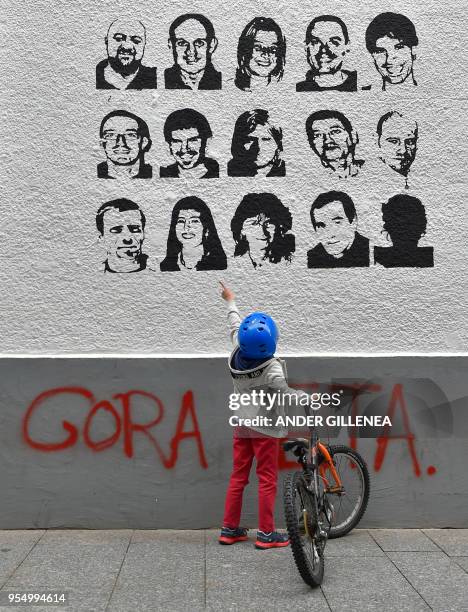 Child holds a bike while pointing at some portraits of Basque separatist group ETA prisoners next to a graffiti meaning "Long life ETA" in the...