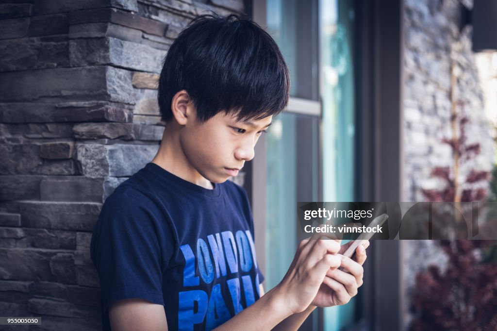 Adolescente muchacho asiático con smartphone, luz al aire libre.