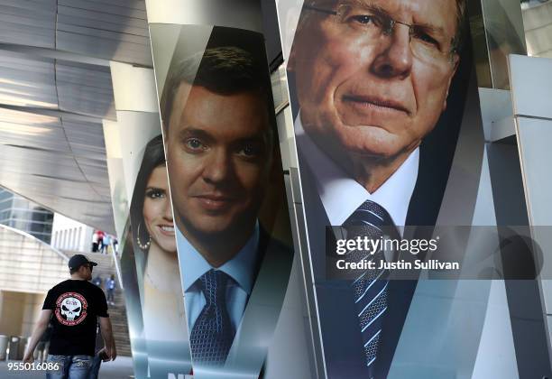 An attendee walks by photographs of National Rifle Association executive vice president Wayne LaPierre, executive Director of the NRA-ILA Chris Cox...