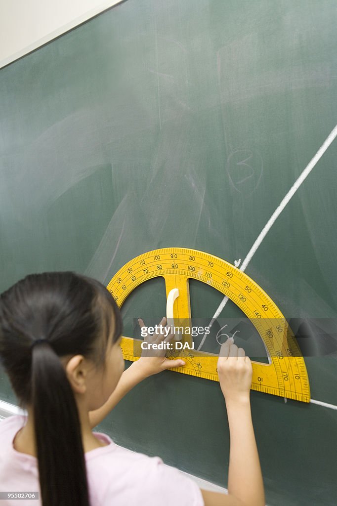 Girl writing with a protractor on blackboard
