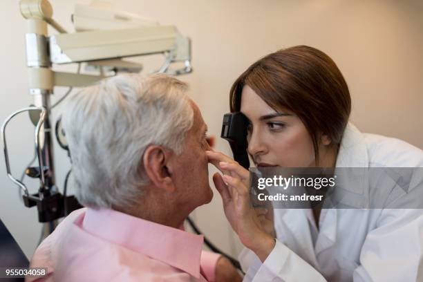 female optometrist checking a senior patient's eyes - astigmatism stock pictures, royalty-free photos & images