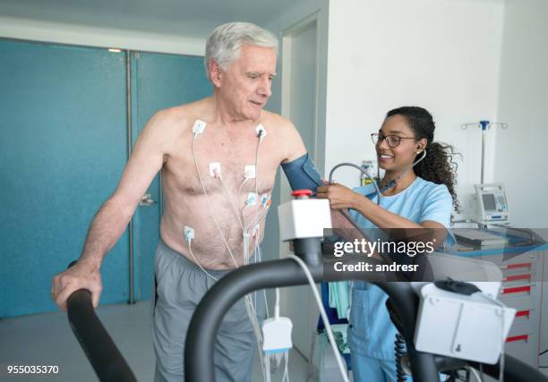 cheerful black nurse checking the blood pressure on a senior patient doing a stress test on a treadmill - diagnostic medical tool stock pictures, royalty-free photos & images