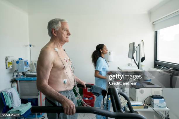 senior man on a treadmill doing a stress test at the hospital while black nurse looks at the cardiac monitor - stress test stock pictures, royalty-free photos & images