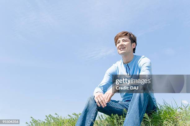 young man sitting on riverbank looking at sky - 河川敷 ストックフォトと画像