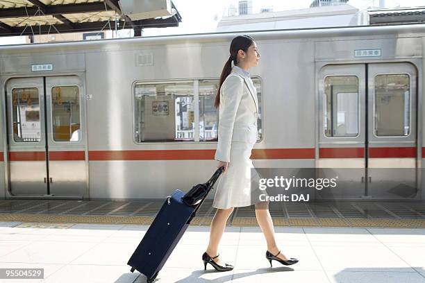 young woman walking at platform, carrying suitcase - ビジネスウーマン　日本 ストックフォトと画像