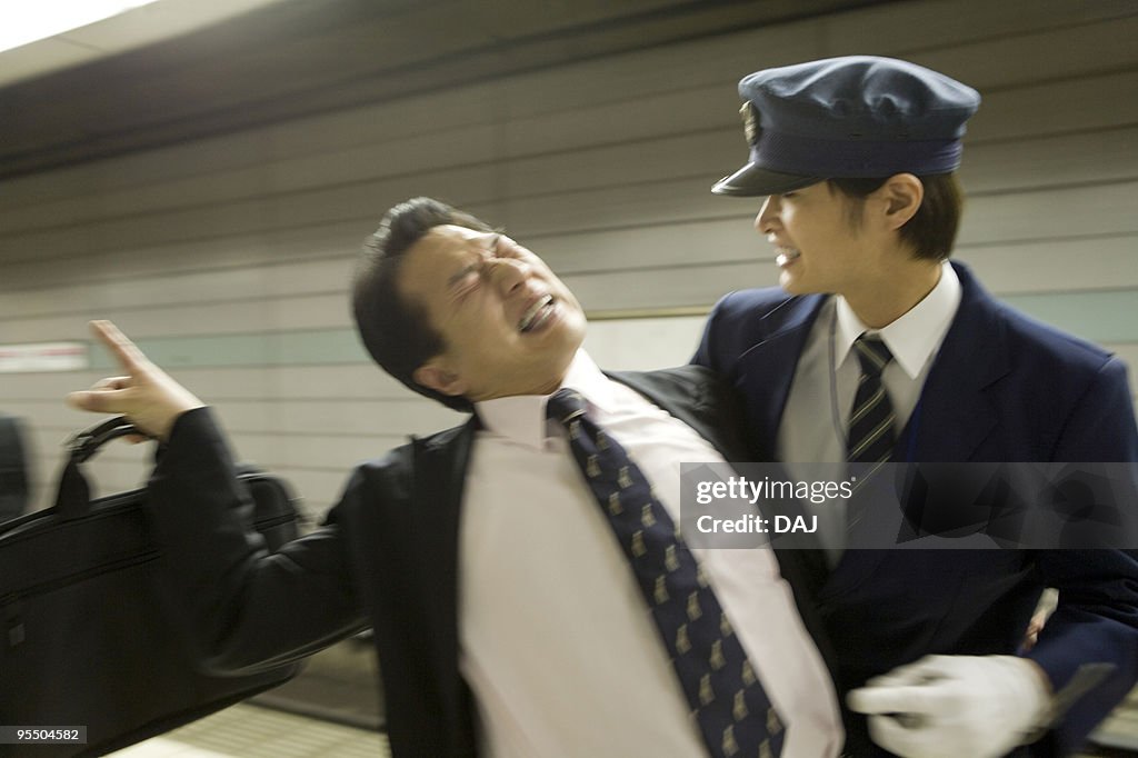 Conductor carrying drunk businessman at platform, blurred motion