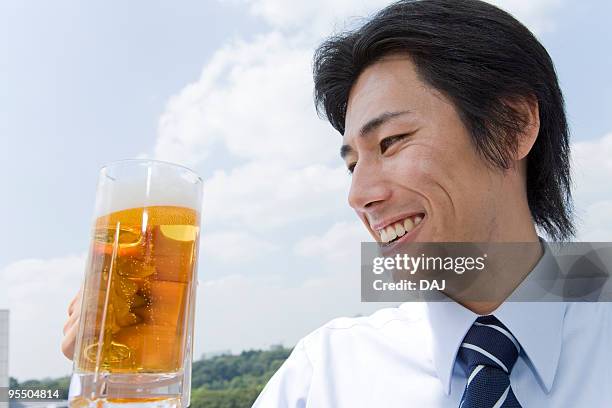 mid adult businessman holding mug of beer - man sipping beer smiling stockfoto's en -beelden