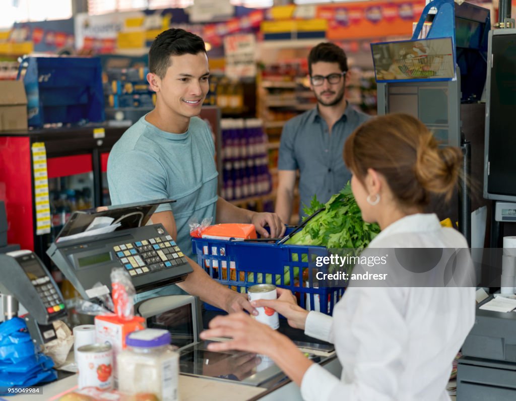 Homem bonito, compras em uma loja de comida e outro cliente esperando para check-out no fundo