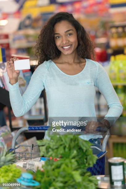 schöne afrikanische amerikanische frau hält eine kundenkarte in einem supermarkt, blick auf die kamera zu lächeln - customer loyalty stock-fotos und bilder