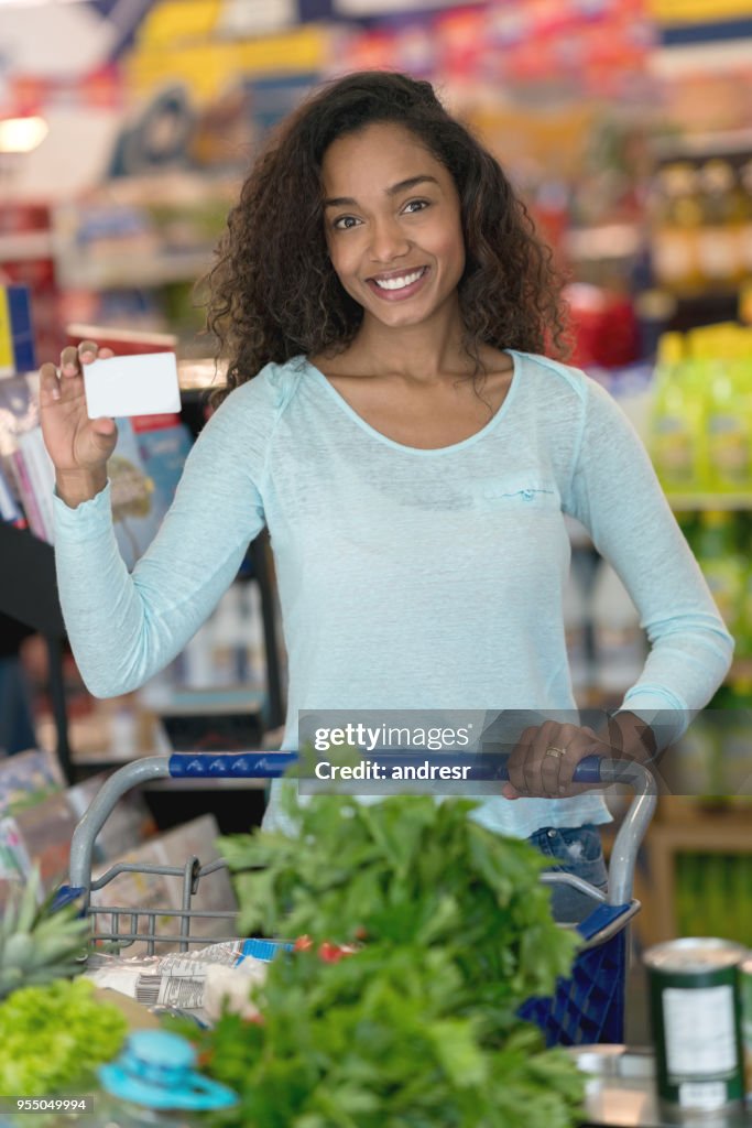 Beautiful african american woman holding a loyalty card at a supermarket looking at camera smiling