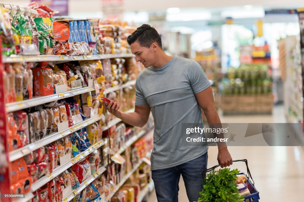 Junge alleinstehende Mann Kauf von Lebensmitteln im Supermarkt lesen das Etikett eines Produkts schauen sehr glücklich