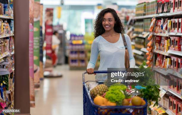 splendida donna nera che compra generi alimentari al supermercato spingendo il carrello della spesa - spingere carrello foto e immagini stock