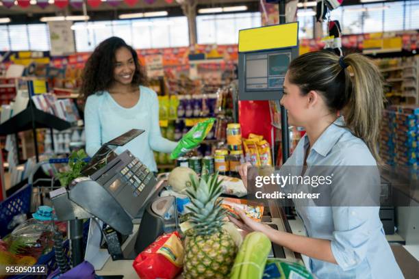 african american woman buying groceries at a supermarket and friendly saleswoman helping with the checkout scanning the products - checkout register stock pictures, royalty-free photos & images