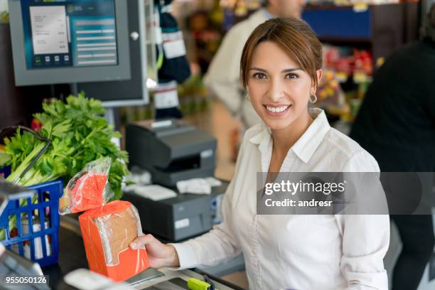freundliche verkäuferin an der kasse, blick in die kamera lächeln beim scannen von barcodes auf produkte - supermarket register stock-fotos und bilder
