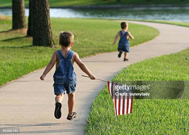 two young boys running in a park with an american flag - 4th of july stockfoto's en -beelden