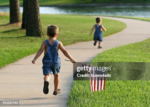 Two young boys running in a park with an American flag