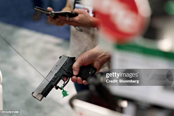 An attendee holds a pistol in a vendor booth during the National Rifle Association annual meeting in Dallas, Texas, U.S., on Saturday, May 5, 2018....