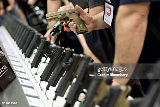 An attendee holds a Fabbrica d'Armi Pietro Beretta SpA pistol at the company's booth during the National Rifle Association annual meeting in Dallas,...