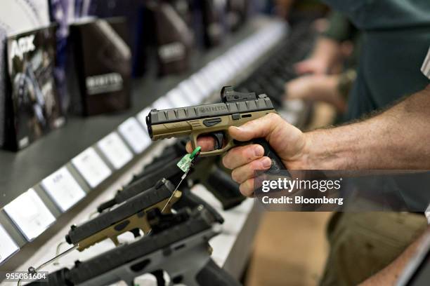 An attendee holds a Fabbrica d'Armi Pietro Beretta SpA pistol at the company's booth during the National Rifle Association annual meeting in Dallas,...