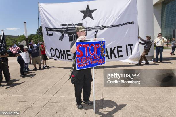 Demonstrator open carries a rifle while holding a sign during a pro-gun rally on the sidelines of the National Rifle Association annual meeting in...