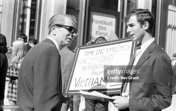 Outside the Time Life Building, a man holds a sign that reads 'Time Inc Employees for Immediate Withdrawal from Vietnam Now' in one hand and a...