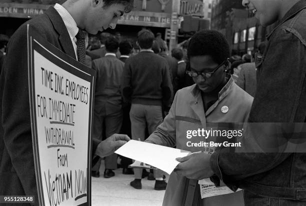 Outside the Time Life Building during the Moratorium to End the War in Vietnam demonstration, a woman signs a petition as she stands between two men,...