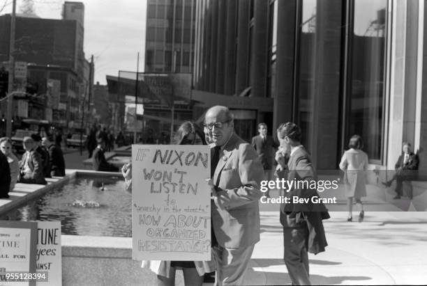 Passerby watches as a young woman holds a sign that reads 'If Nixon Won't Listen to Anarchy in the Streets, How About Organized Resistance?'outside...