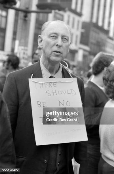 View of an man, with a sign around his neck that reads 'There Should Be No Fighting,' as he stands outside the Time Life Building during the...