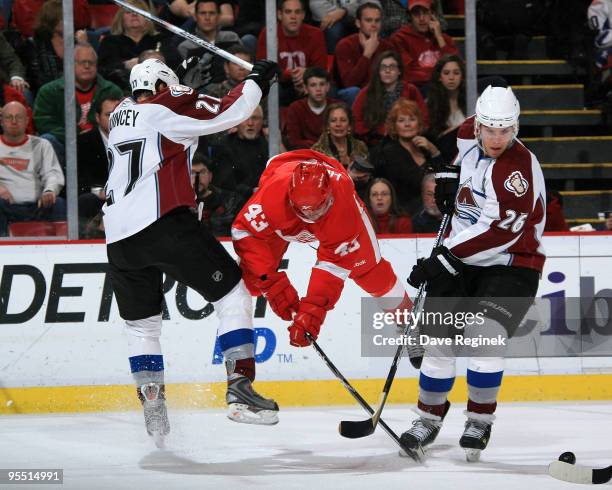 Paul Stastny of the Colorado Avalanche and teammate Kyle Quincey look for the loose puck as Darren Helm of the Detroit Red Wings flys through mid-air...