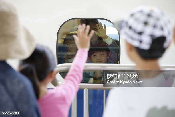 Young passenger waves from the window of a shinkansen bullet train at JR Shin-Osaka Station on May 6 the final day of Japan's Golden Week holidays....