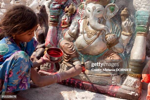 Une petite fille travaille à la peinture des statues dans le quartier des potiers, Delhi, Inde. Elle peint avec précision le dieu éléphant, Ganesh.