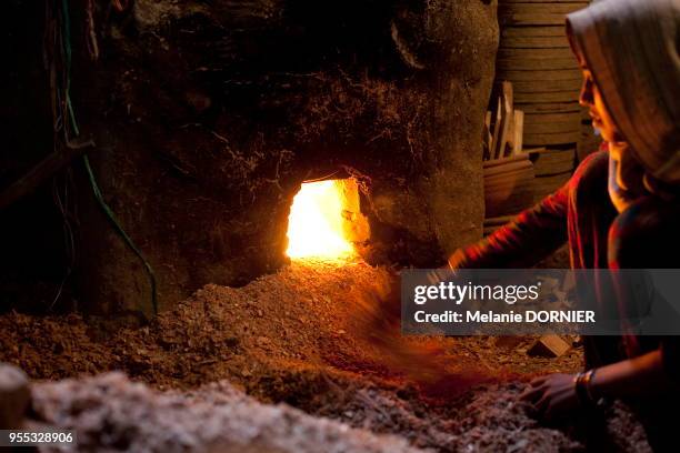 Une femme alimente le feu qui sert a cuire les objet de terre dans le village de potiers , New Delhi, Inde.