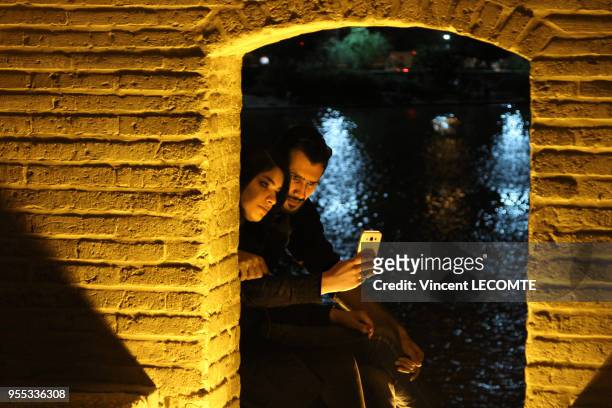 Un couple d?amoureux examine leur selfie sur leur téléphone sous une arcade du pont Si-o-se Pol à Ispahan, Iran, en avril 2015 - A la nuit tombée, ce...