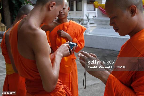 En attendant le début de la cérémonie de la prière du soir, des moines bouddhistes asiatiques en tenue traditionnelle comparent leurs photographies...