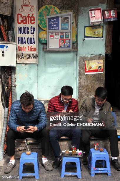 Jeunes gens prenant un verre et consultant leurs téléphones portables dans un café vietnamien typique, reconnaissable à ces mini tabourets et tables...