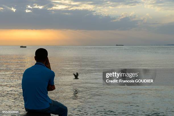 Homme de dos téléphonant en regardant le coucher du soleil depuis le Molo Audace, le 10 août 2017, Trieste, Italie.