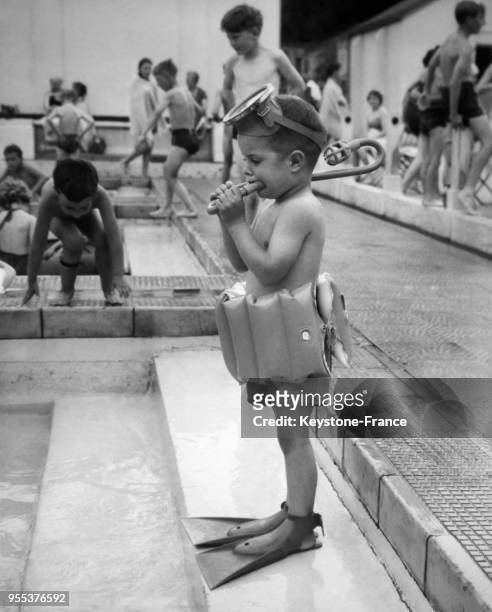 Un petit enfant arrivé du Canada et équipé de bouée et de palmes sur le bord de la piscine à Roehampton, Royaume-Uni.