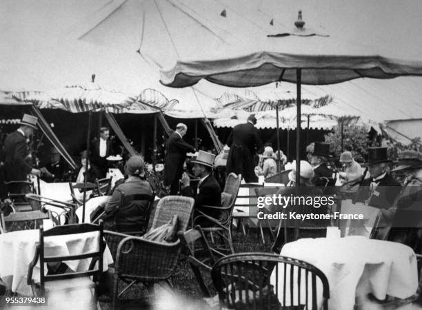 Des spectateurs en tenue élégante assis aux tables sous les parasols du carré de la Cavalerie à Ascot, Royaume-Uni.