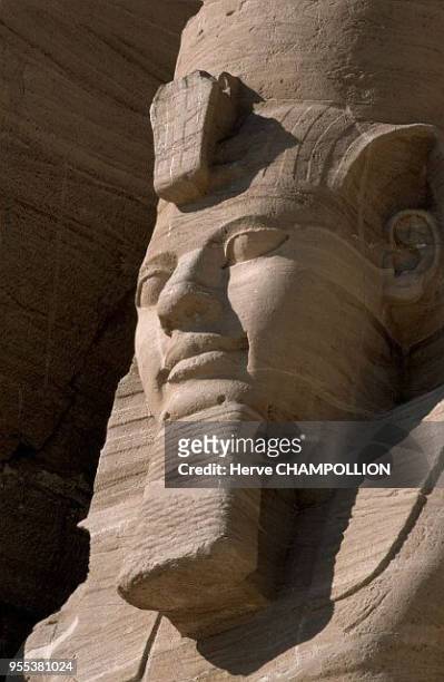 Before the facade of the temple in the mountain, four colossi of Ramses II stand guard. The king wears the double "pschent" crown here over his...