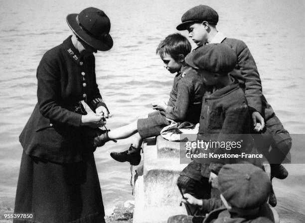 S Femme policière refaisant les lacets de chaussure d'un enfant sur les quais de la Tamise à Londres, Royaume-Uni.