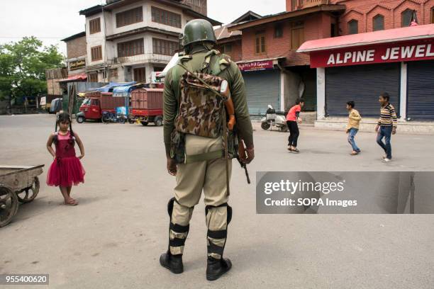 Children play as an Indian paramilitary trooper stands alert during the restrictions imposed by authorities in Srinagar, the summer capital of Indian...