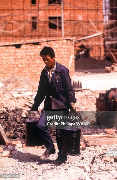 Ouvrier transportant des seaux de goudron sur un chantier à Pékin, Chine.