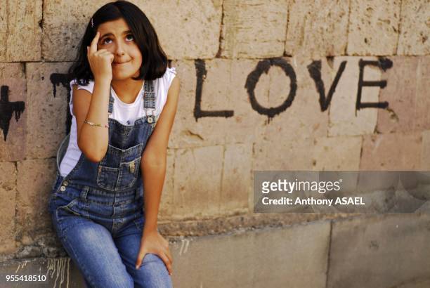 Armenia, Yerevan, Armenian girl with jeans leaning to a stone wall with love writing and day dreaming.