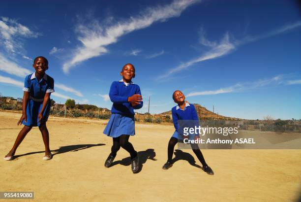 Africa, Lesotho, Maseru, three schoolgirls in blue school uniform dancing on ground with mountain in the background.