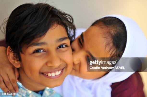 Close-up portrait of a school girl kissing her friend in joy , Muscat, Oman.