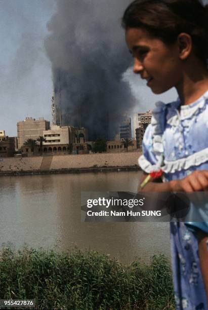 A little girl is walking around her house while on the other side of the river, the Iraqi telecommunications building is still burning after the May...