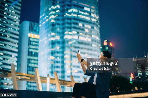 young female traveller capturing the city night scene with smartphone in downtown area - woman capturing city night foto e immagini stock